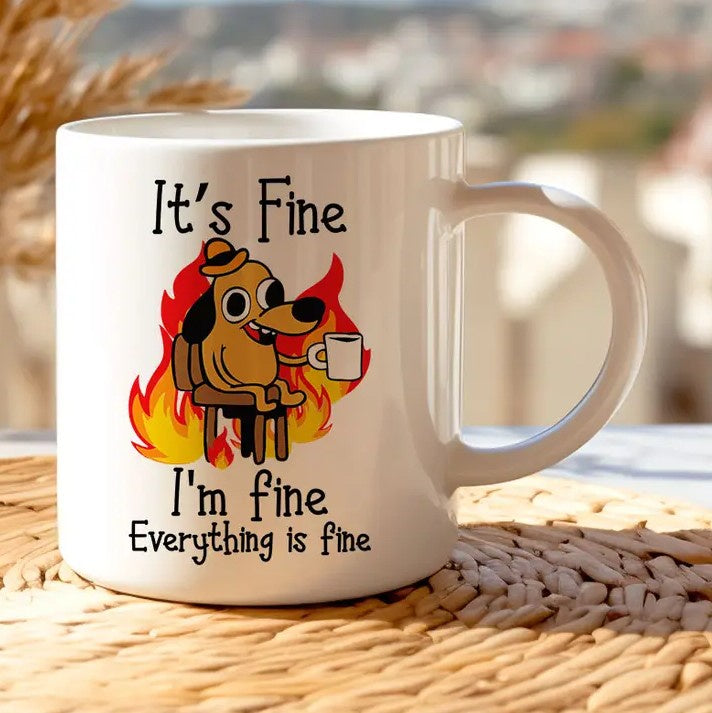 White mug featuring a cartoon dog holding a mug in front of a fiery background with text "It's fine. I'm fine. Everything is fine."