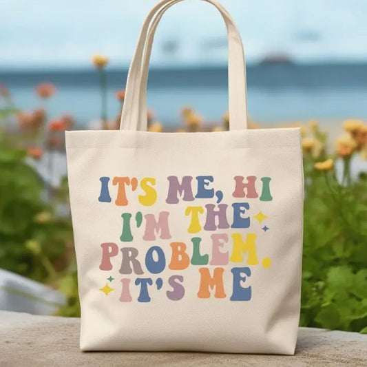 A tote bag that reads "It's Me, Hi, I'm the Problem, it's Me" in a bubbly and colorful font.