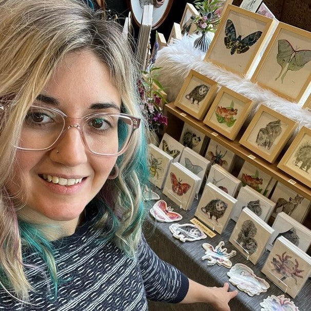 Artist Jen Toledo in front of a table of her art prints and stickers