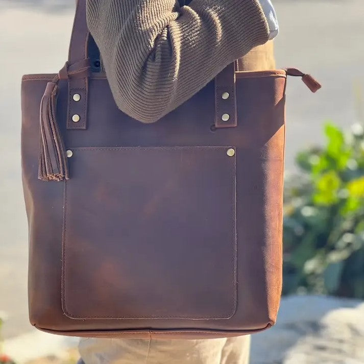 A brown leather tote bag with a tassel. 