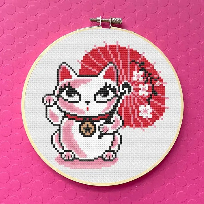 Cross-stitched design of a lucky cat holding a red parasol 