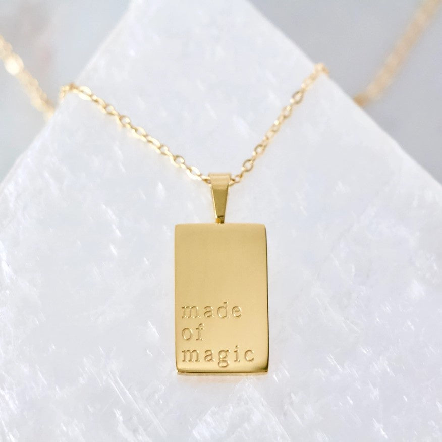 gold necklace with small rectangular pendant inscribed with the words "made of magic"