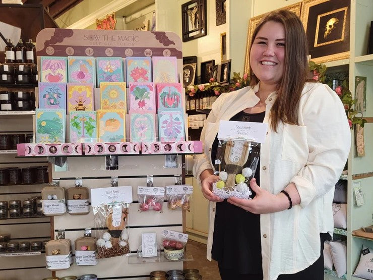 Maria of Almas and Co. holding a bag of seed bombs and standing in front of a shelf of seed kits.