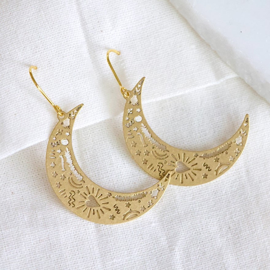 Dangling gold earrings shaped like crescent moons etched with hearts and squiggles