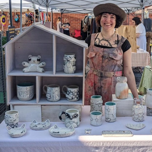 Artist Molly standing behind a table of her handmade pottery