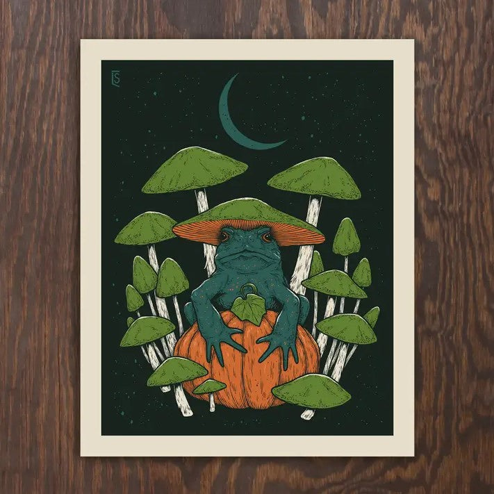 An 8x10 print of a dark green frog with a mushroom cap on its head surrounded by green toadstools and perched atop a small orange pumpkin.