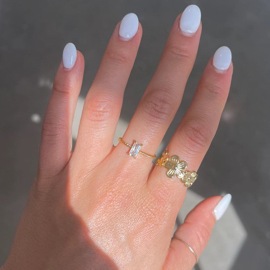 A delicate ring with a thin twisted gold band and a small rectangular white gemstone at the center.