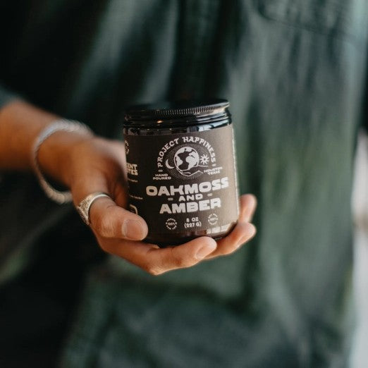 Person holding a jar labeled 'Oakmoss and Amber' by Project Happy