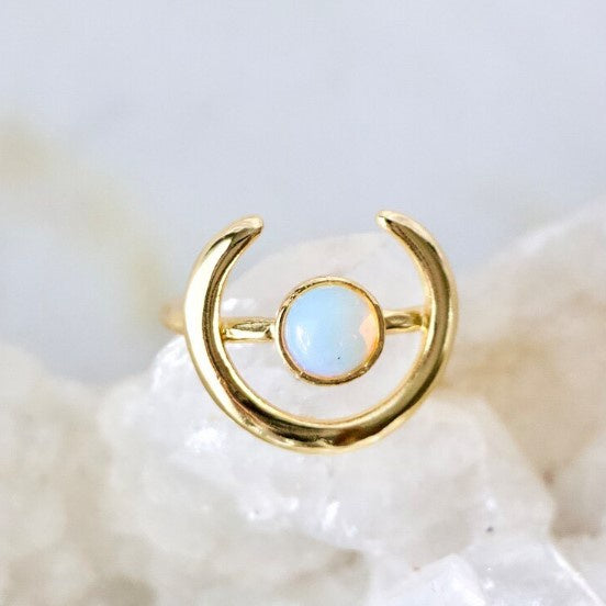 An adjustable gold ring with a circular opalite gem encircled by a horseshoe shape.