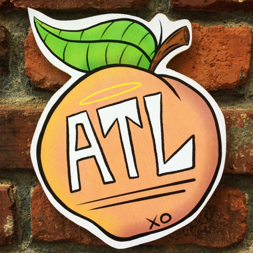 Wooden wall art featuring a peach with "ATL" written on it in a large handwritten font and a small yellow halo above the word