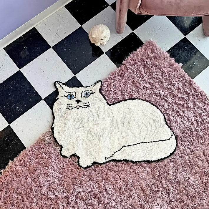 Small rug in the shape of a white Persian cat with blue eyes and a pink tongue lying down.