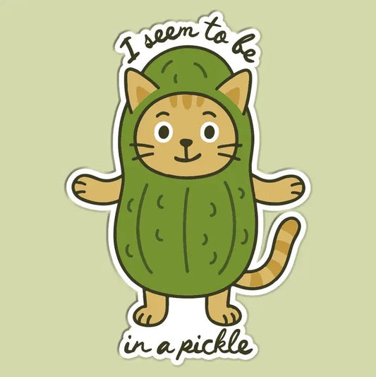 A sticker depicting a smiling orange cat wearing a pickle costume with cursive font "I seem to be in a pickle"