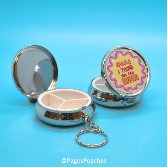 Silver pill organizer key chain with a pink and yellow funky design on the front