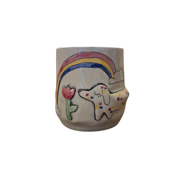White ceramic cup with a tulip, rainbow and polka dotted dog painted on it