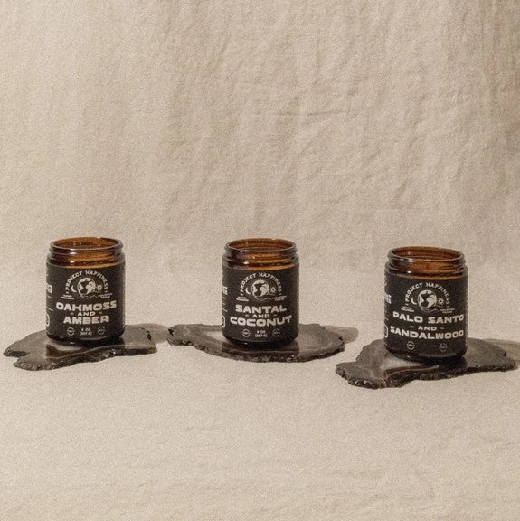 Three candles in glass jars with labels on a textured beige background