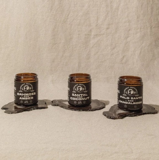 Three candles in glass jars with labels on a textured beige background