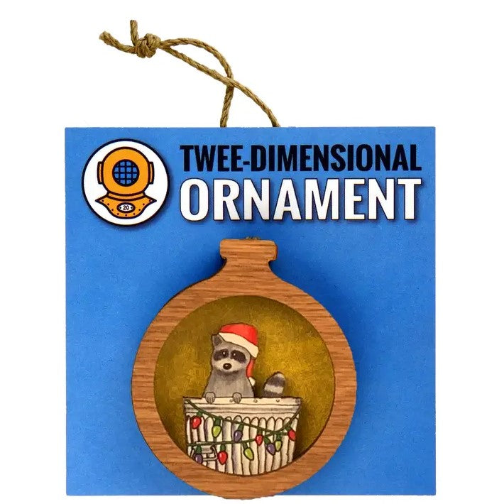 A circular wooden Christmas ornament featuring a raccoon in a Santa hat peeking out of a trash can wrapped in Christmas lights