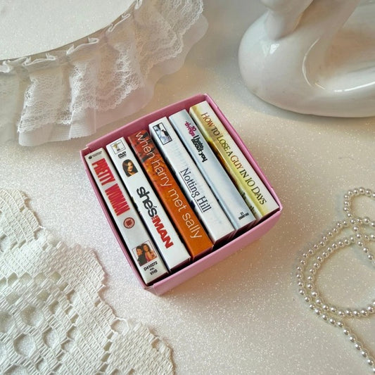 A pink rectangular box containing six matchbooks designed like rom com DVD cases