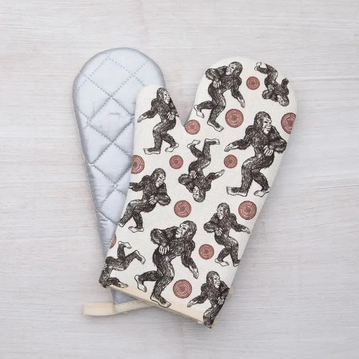 An oven mitt covered in images of a sasquatch and aerial views of a tree stump.