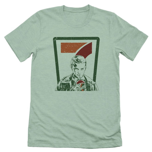 Light green t-shirt with the 7-11 logo behind Eleven from Stranger Things sipping a large drink