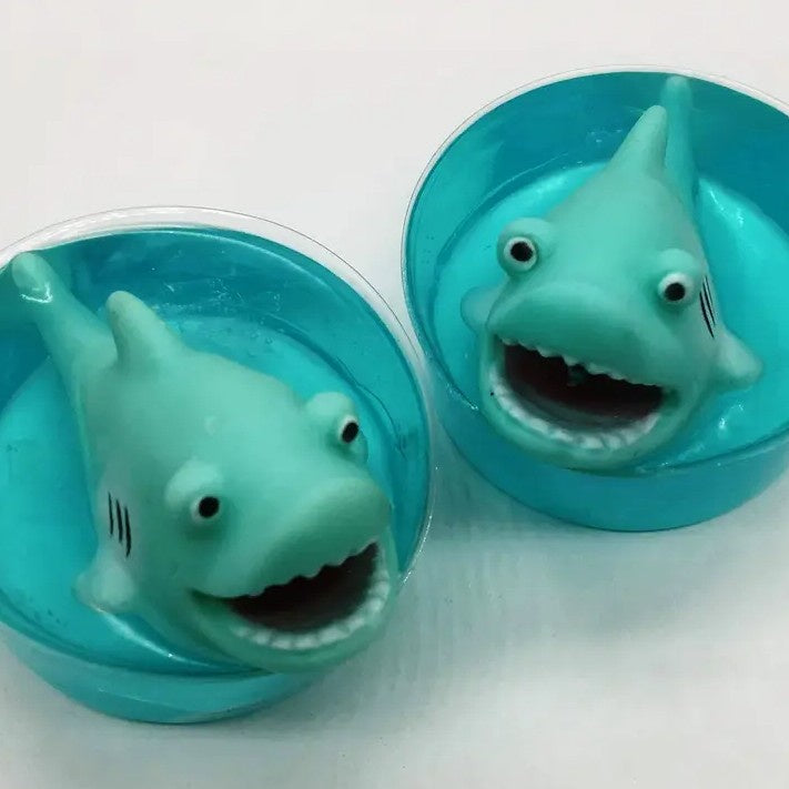 Two round turquoise soap bars with shark toys inside