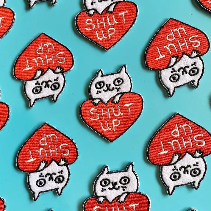 Fabric patch featuring a white cat peeking over a red heart that reads "Shut Up"