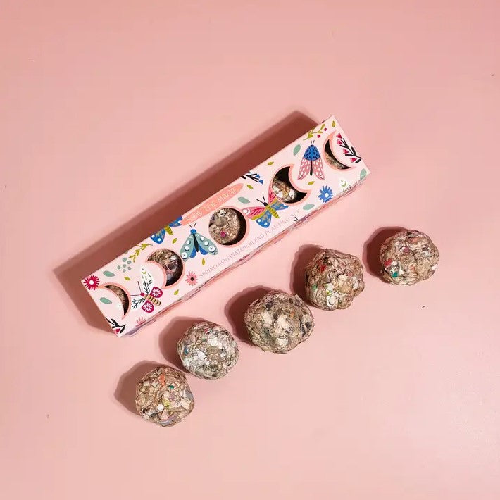 Five seed balls consisting of spring pollinator plants in a pink cardboard box decorated with butterflies and moon phases.