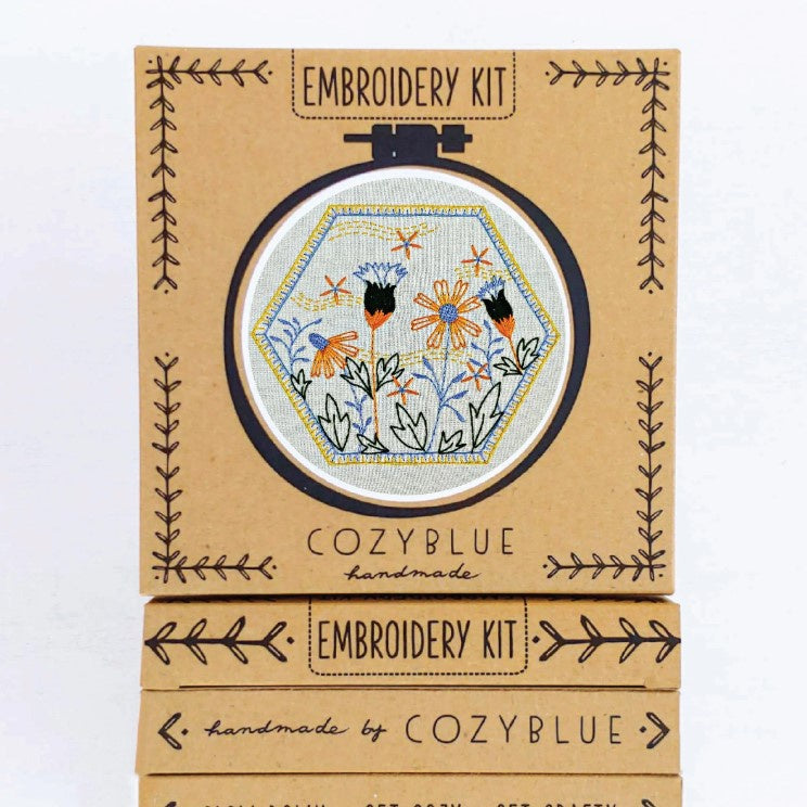 An embroidery kit depicting yellow, blue and black daisies with a hexagonal stitched frame around them.