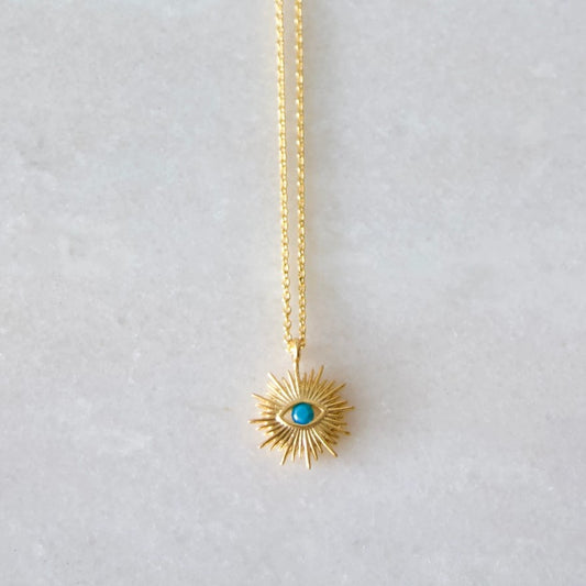 a gold necklace with a gold pendant shaped like a sun with a blue eye at the center