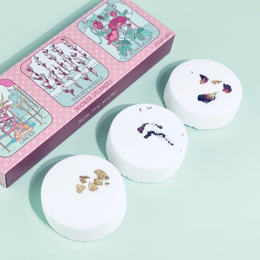 Three white bath bombs with floral designs on a light green background, accompanied by a decorative box.