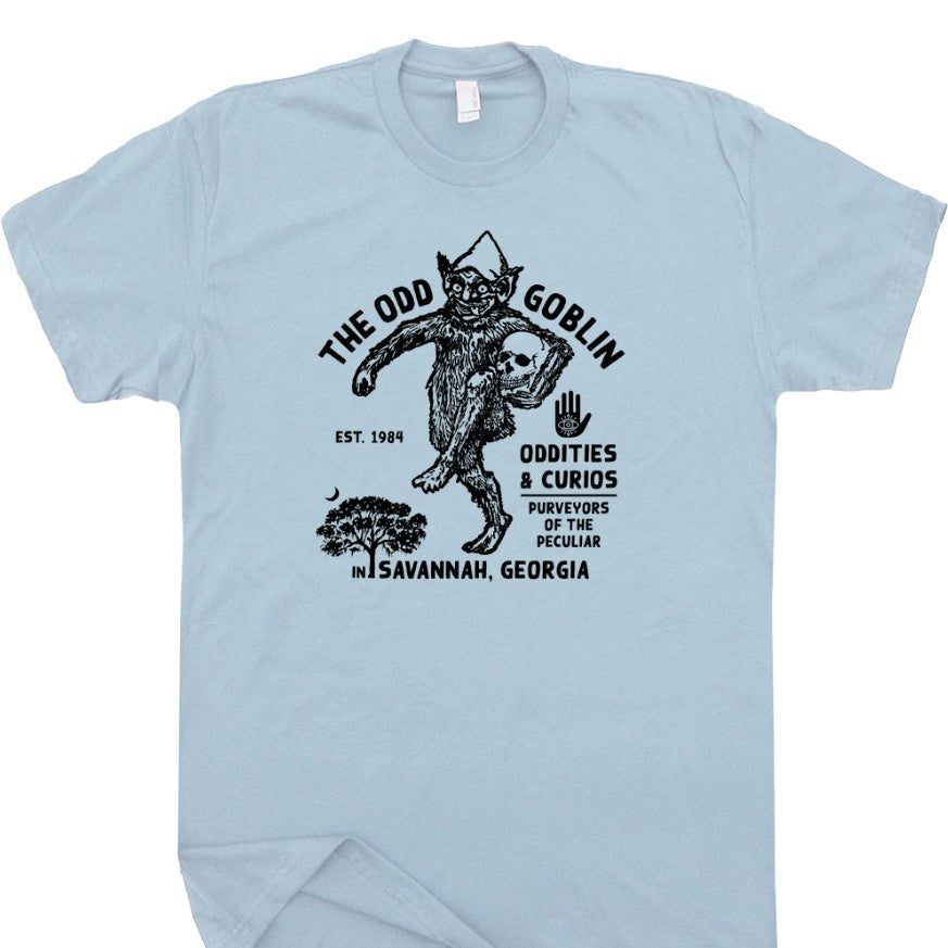 Light blue tee shirt with a graphic of a skipping goblin and text that reads "The Odd Goblin Oddities and Curios"