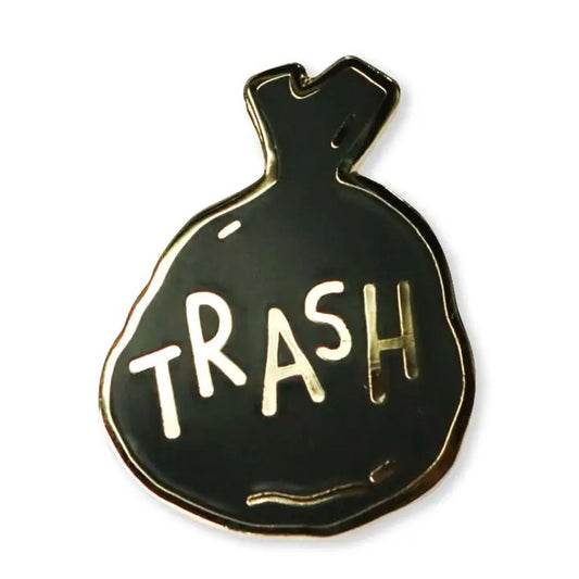 Enamel pin in the shape of a black trash bag with the word "Trash" on it