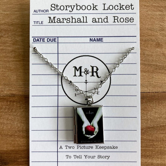 A locket designed to look like the book Twilight with two hands cupping a red apple on the front cover.