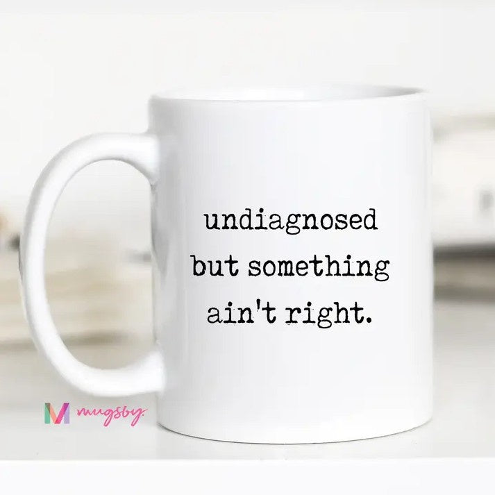 White mug with black text that reads "undiagnosed but something ain't right."