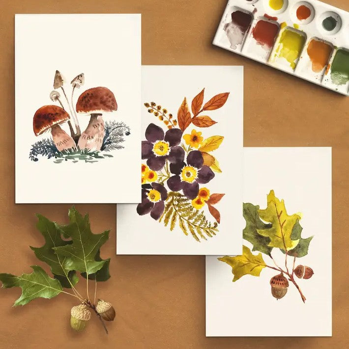 Four watercolor illustrations of nature-themed designs on a brown surface with paint palette.