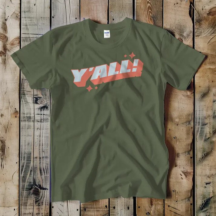 A green tee shirt with the word "Y'ALL!" written in a graphic font with an orange drop-shadow and sparkles around it.