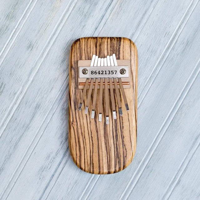 Striped wooden kalimba with metal tines on a light gray wooden surface
