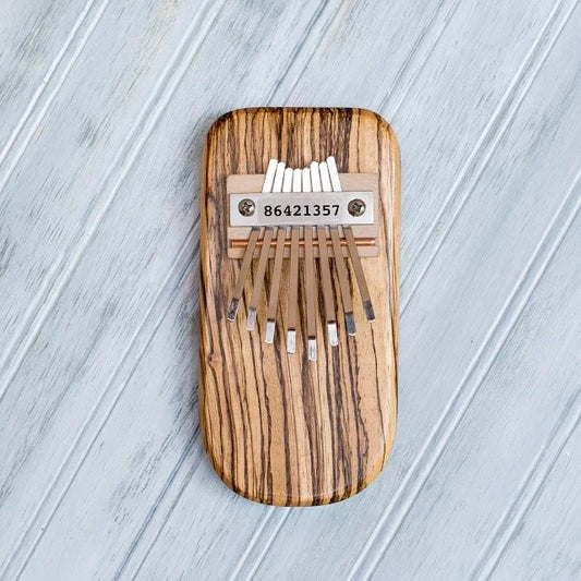 Striped wooden kalimba with metal tines on a light gray wooden surface