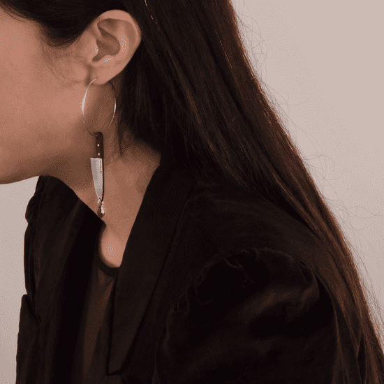 women wearing silver hoop earrings with an attached knife and a bloody gemstone