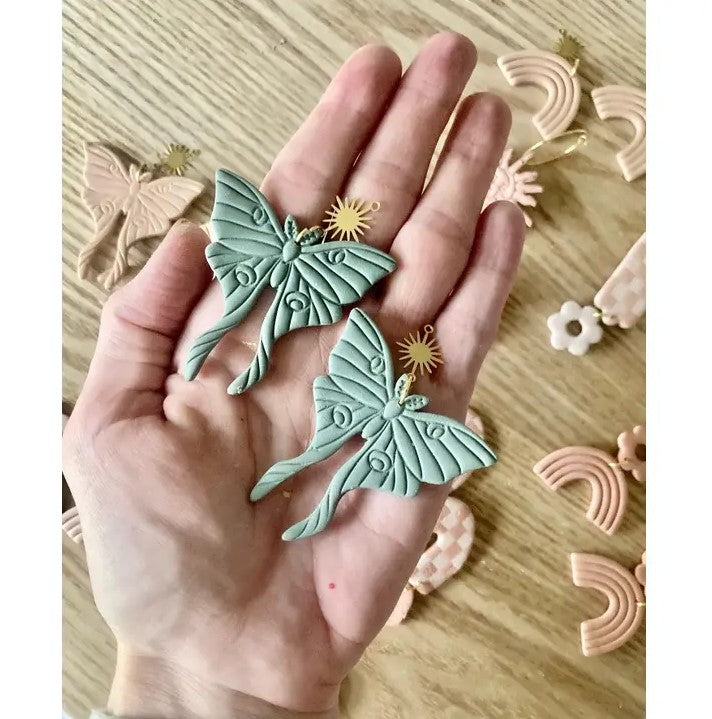 Hand holding handmade clay luna moth earrings with gold accent charm