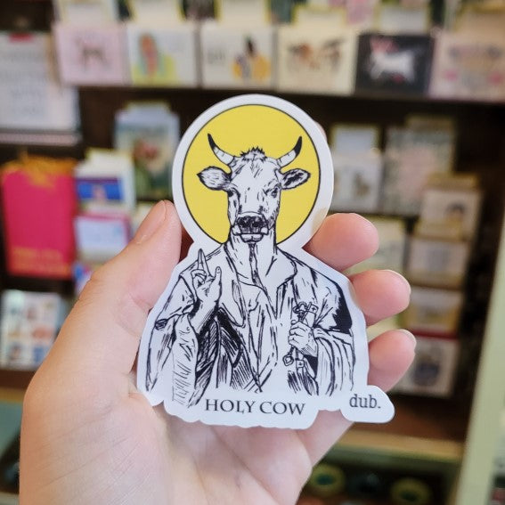 Hand holding sticker that features a cow and the quote "Holy cow"