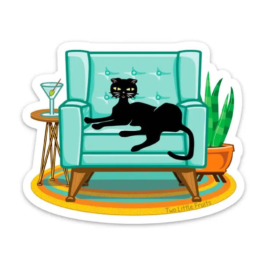 Black Cat sitting on a blue couch with a martini glass to the left on a side table and a succulent to the right